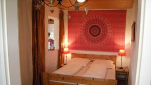 Een houten bed met twee kussens, een rode wandtapijt met patroon en twee bedlampen.