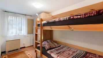 Une chambre avec un lit superposé doté d’une tête de lit en bois, un petit bureau avec une lampe, un radiateur et un tapis à motifs.
