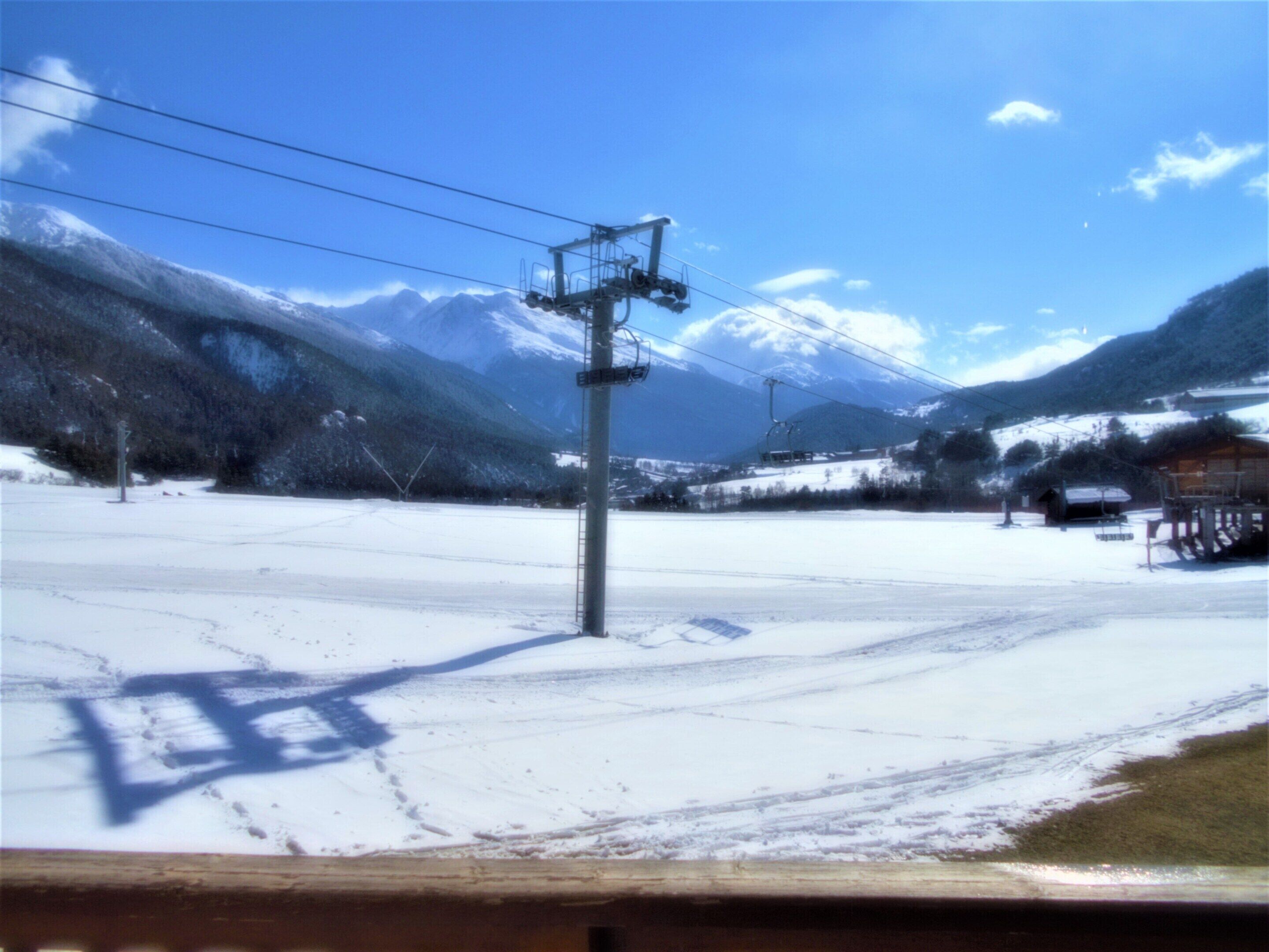 A snow-covered landscape with a ski lift, mountains, and a wooden cabin.