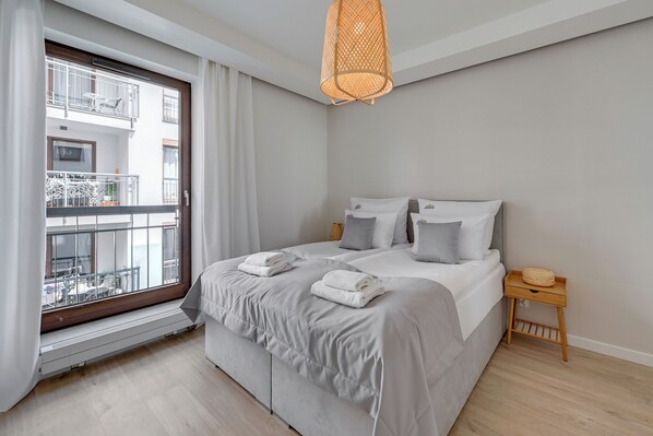 A bedroom with a large bed, a window with a view of a balcony, a small wooden nightstand, and a woven light fixture. - Riverside Szafarnia Street by Downtown Apartments (Gdansk)