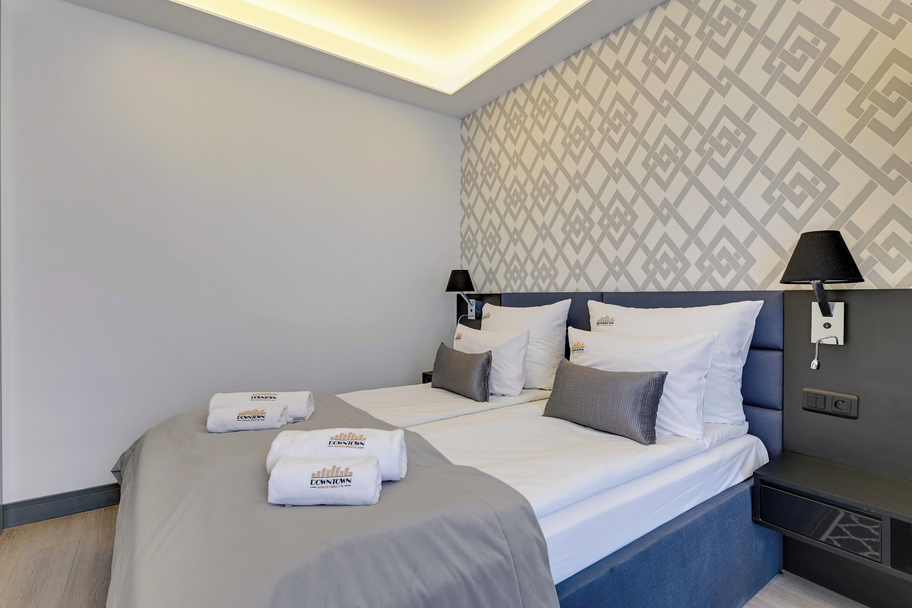 A hotel room with a bed, two bedside tables, a wall-mounted lamp, and a patterned wallpaper.
