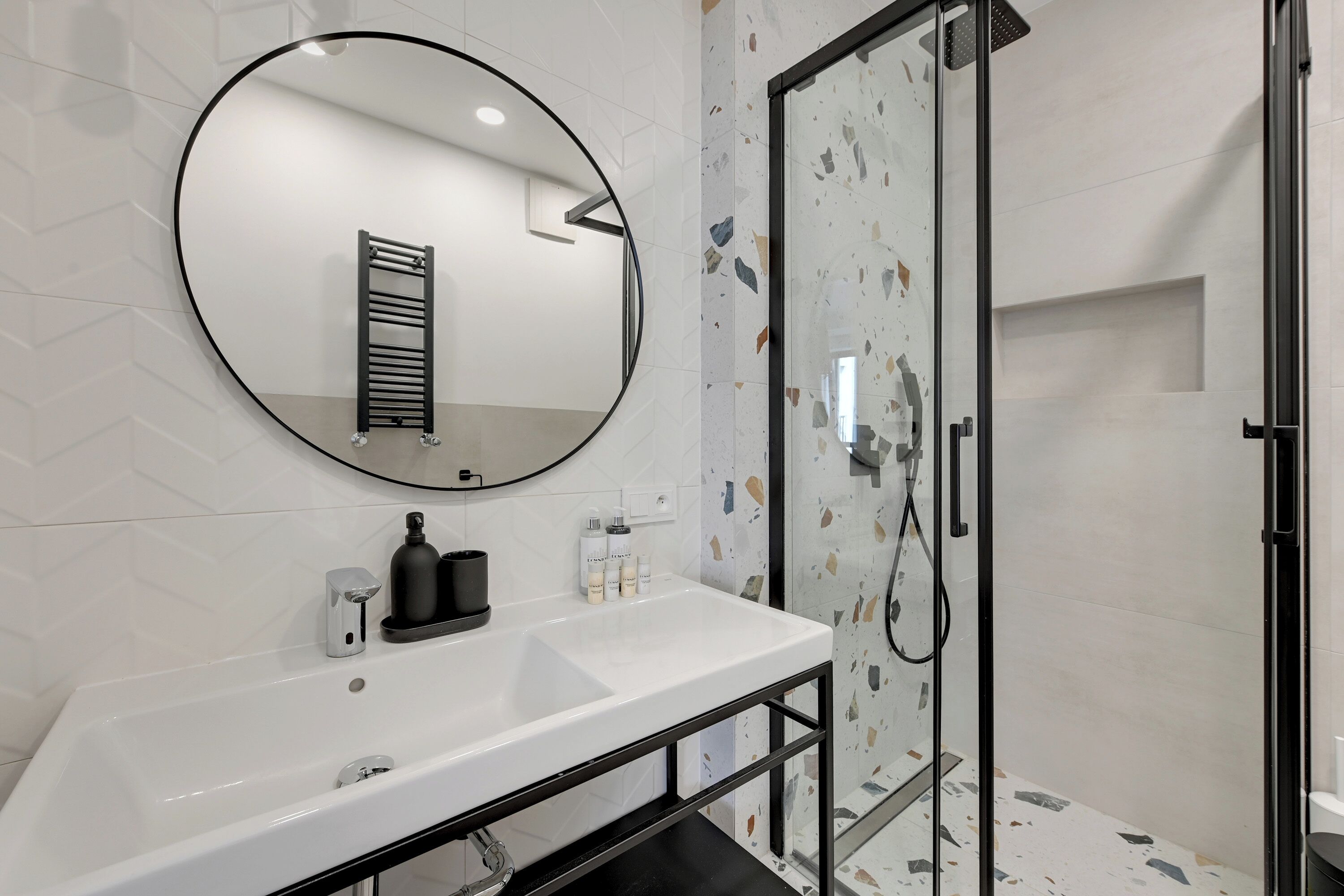 Une salle de bain moderne avec un lavabo blanc, un miroir rond et une douche à parois de verre.