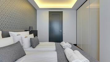 A modern hotel room with a neatly made bed, a grey and white color scheme, and a patterned wall.