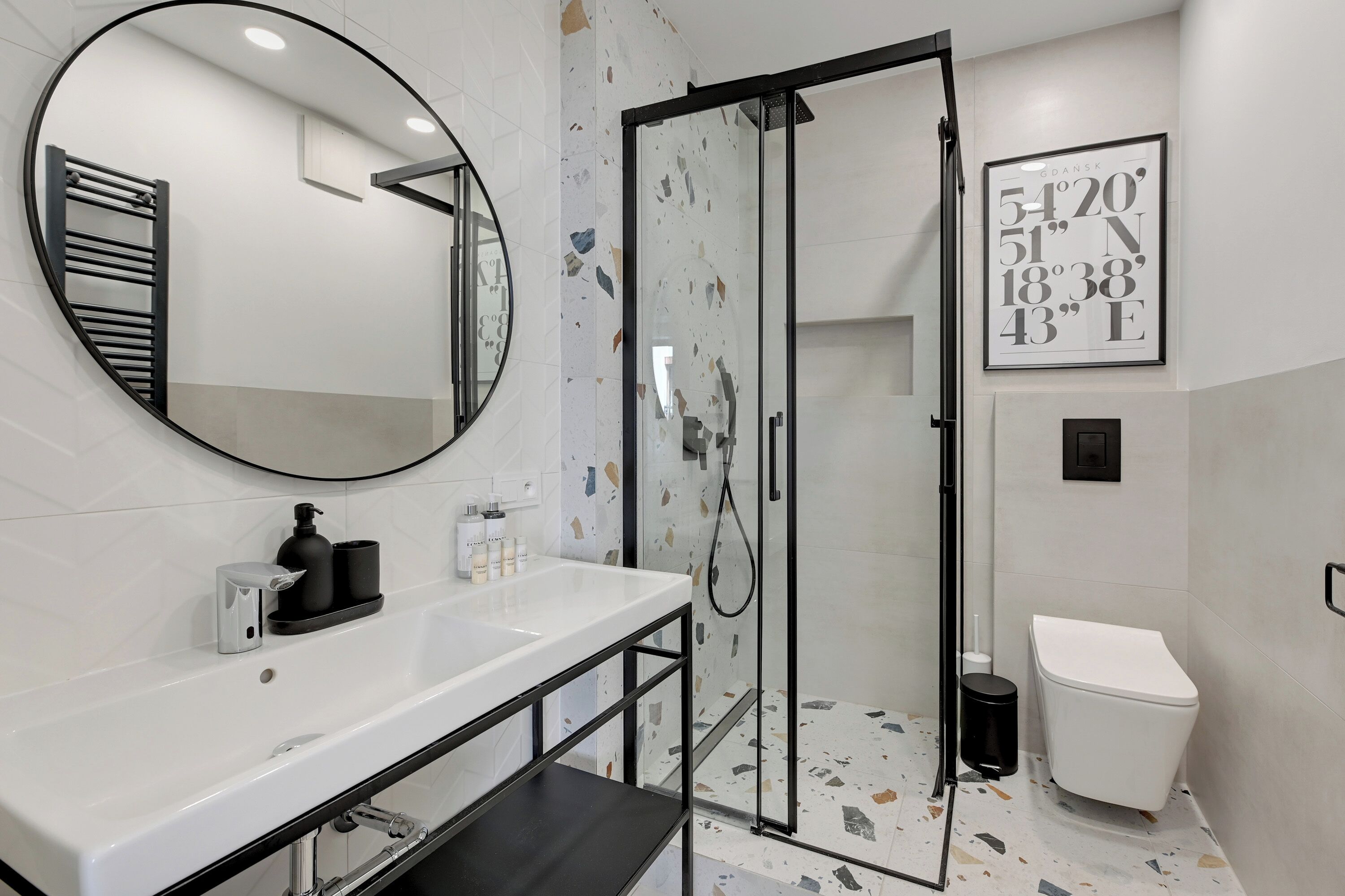 Une salle de bain moderne avec un lavabo blanc, un porte-serviettes noir et une cabine de douche en verre.