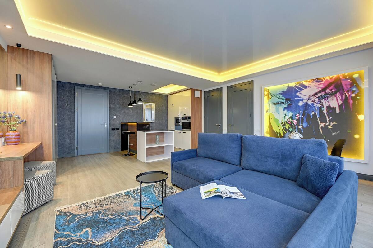 A modern living room with a blue sofa, a small side table, and a colorful abstract painting on the wall.