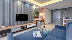 A modern living room with a flat-screen TV, a sofa, a coffee table with a magazine, and a kitchen area in the background. - Riverside Szafarnia Street by Downtown Apartments (Gdansk)