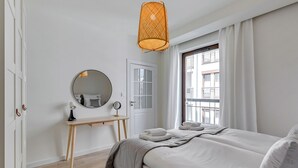 A bedroom with a bed, a bedside table with a lamp, a mirror, and a window with curtains. - Riverside Szafarnia Street by Downtown Apartments (Gdansk)