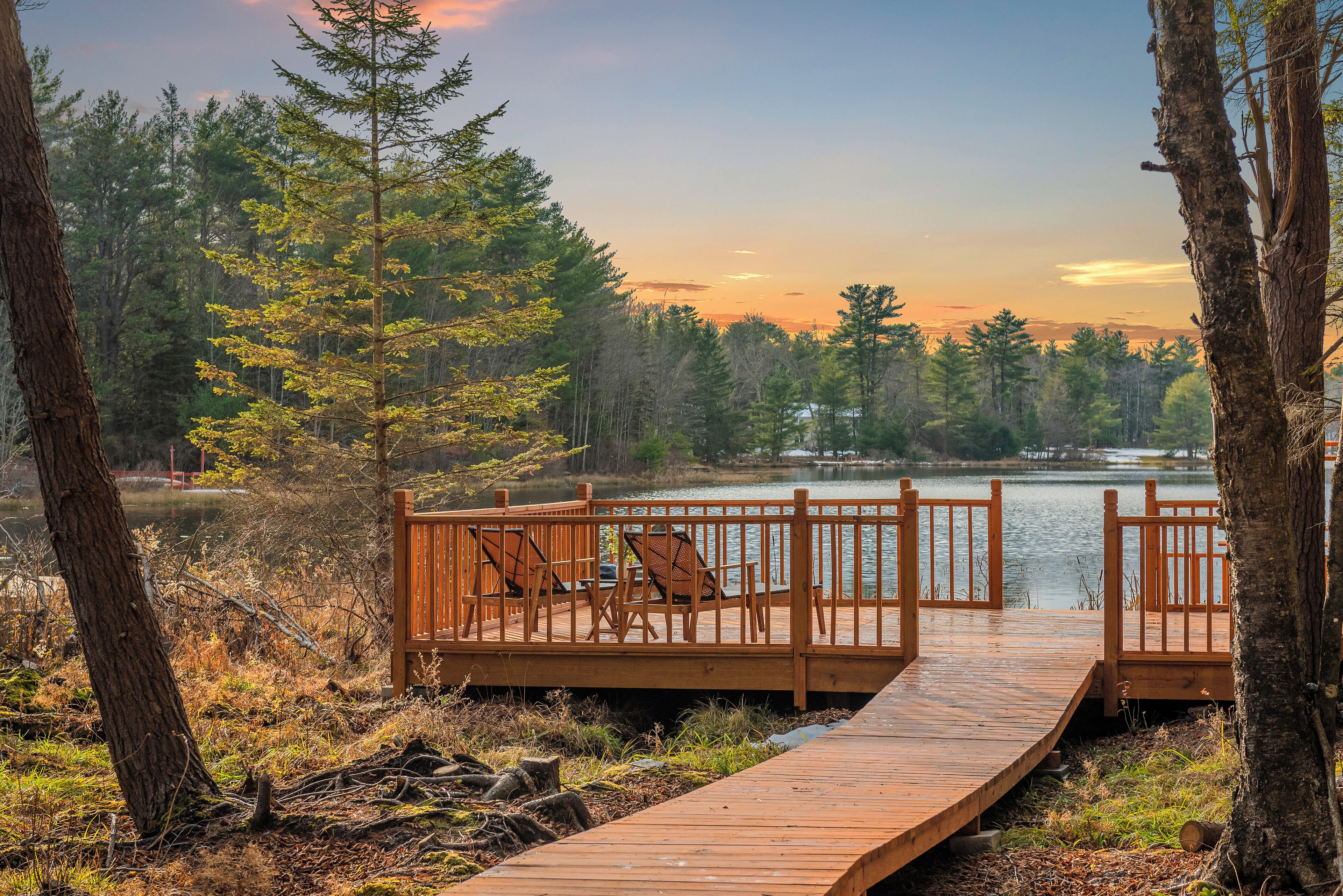 Eine Holzterrasse mit Stühlen, die auf einen See mit Baumumrandung blickt.