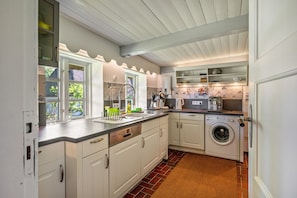 A kitchen with white cabinets, a dishwasher, a washing machine, and a window with a view of greenery. - Vacation home 'Poppenstuuv', idyllic baroque fairytale garden, sauna, parking, Wi-Fi (Stadum)