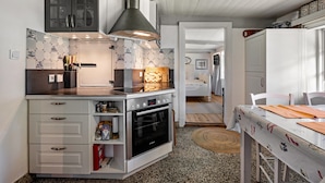 A compact kitchen with a built-in oven, a stainless steel range hood, and a dining area with a table and chairs. - Vacation home 'Poppenstuuv', idyllic baroque fairytale garden, sauna, parking, Wi-Fi (Stadum)