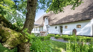 A white building with a thatched roof, surrounded by lush greenery and a well-maintained garden. - Vacation home 'Poppenstuuv', idyllic baroque fairytale garden, sauna, parking, Wi-Fi (Stadum)