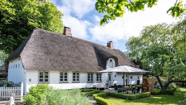 A white building with a thatched roof, a garden with a paved path, and outdoor seating. - Vacation home 'Poppenstuuv', idyllic baroque fairytale garden, sauna, parking, Wi-Fi (Stadum)