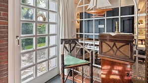 A room with a large window, a wooden chair, a desk with a radio, and a brick wall. - Vacation home 'Poppenstuuv', idyllic baroque fairytale garden, sauna, parking, Wi-Fi (Stadum)