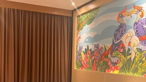 A hotel room with a large bed, a chair, a mural with birds and flowers, and a window with curtains. - Alltrue Hotel Palangkaraya (Palangkaraya)