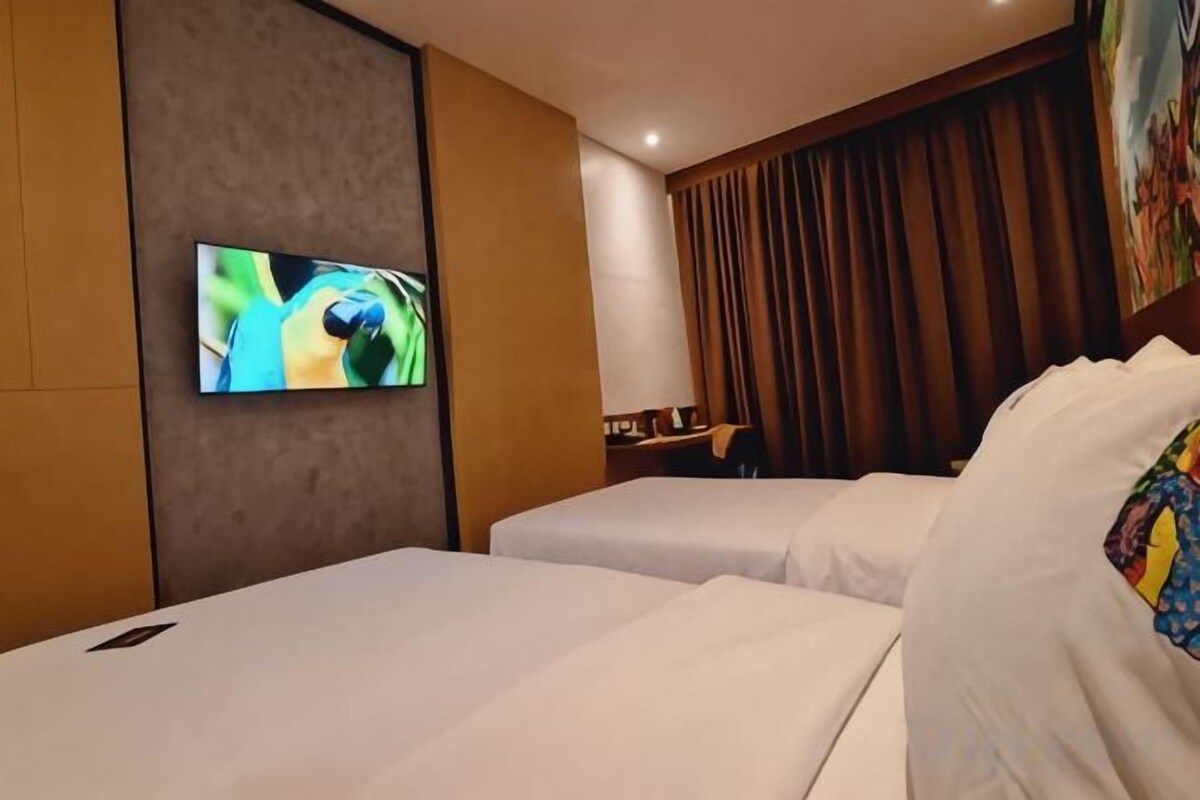 A hotel room with two beds, a flat-screen TV mounted on the wall, and a large window with curtains.
