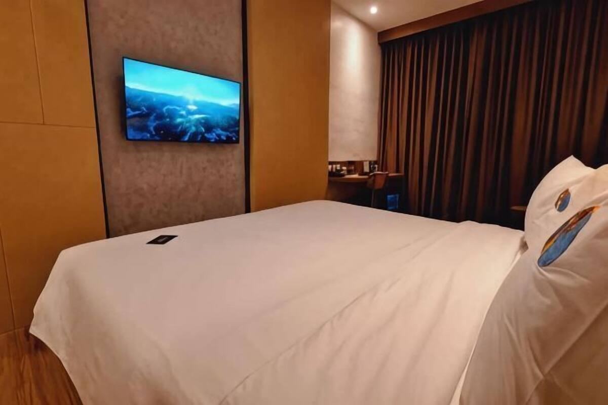 Une chambre d’hôtel équipée d’un lit, d’un téléviseur à écran plat fixé au mur, d’un bureau et d’une fenêtre avec des rideaux.