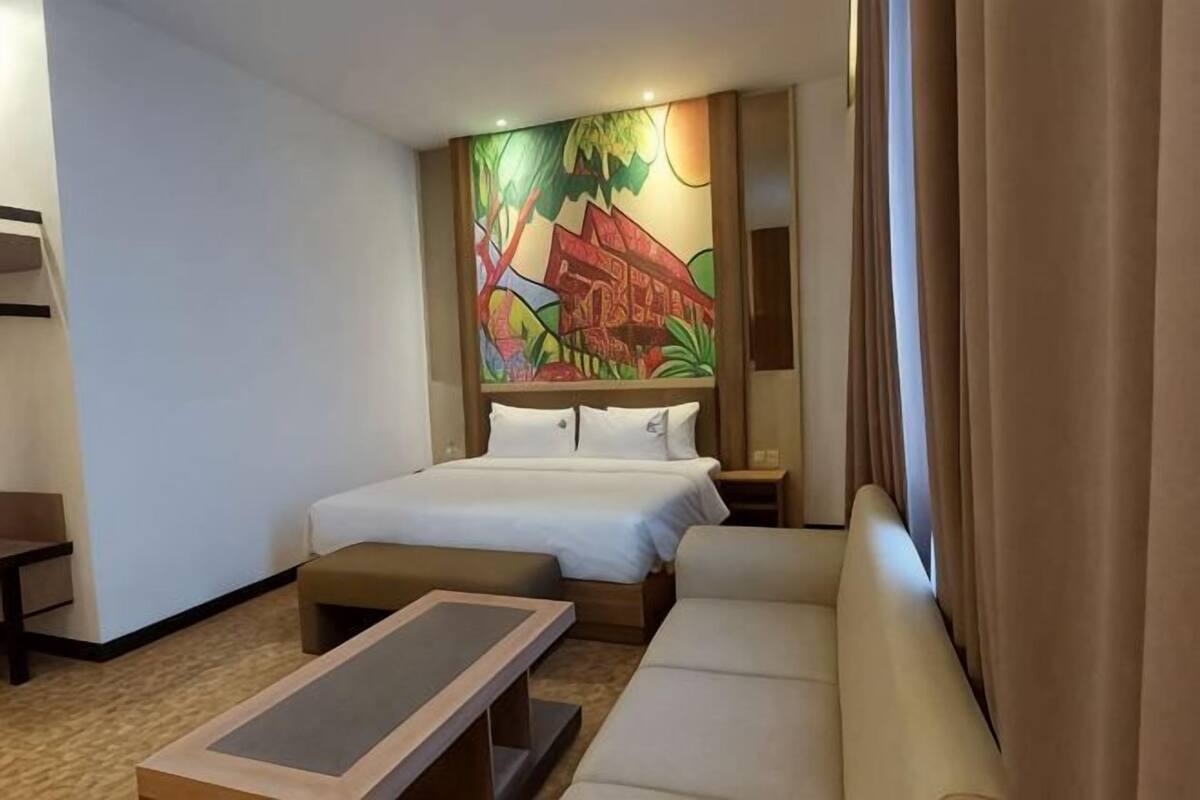 Une chambre d’hôtel avec un lit, un canapé, une petite table et une fresque colorée sur le mur.
