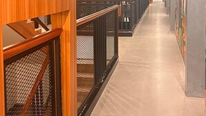 A corridor with wooden paneling and metal railings, leading to a staircase with a view of the upper floor. - Alltrue Hotel Palangkaraya (Palangkaraya)