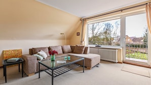 A living room with a sofa, a glass coffee table, a radiator, and a large window with curtains.