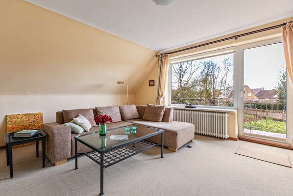 A living room with a sofa, a glass coffee table, a radiator, and a large window with curtains.
