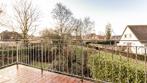 A balcony with a metal railing, brick flooring, and a view of a residential area with houses and trees.