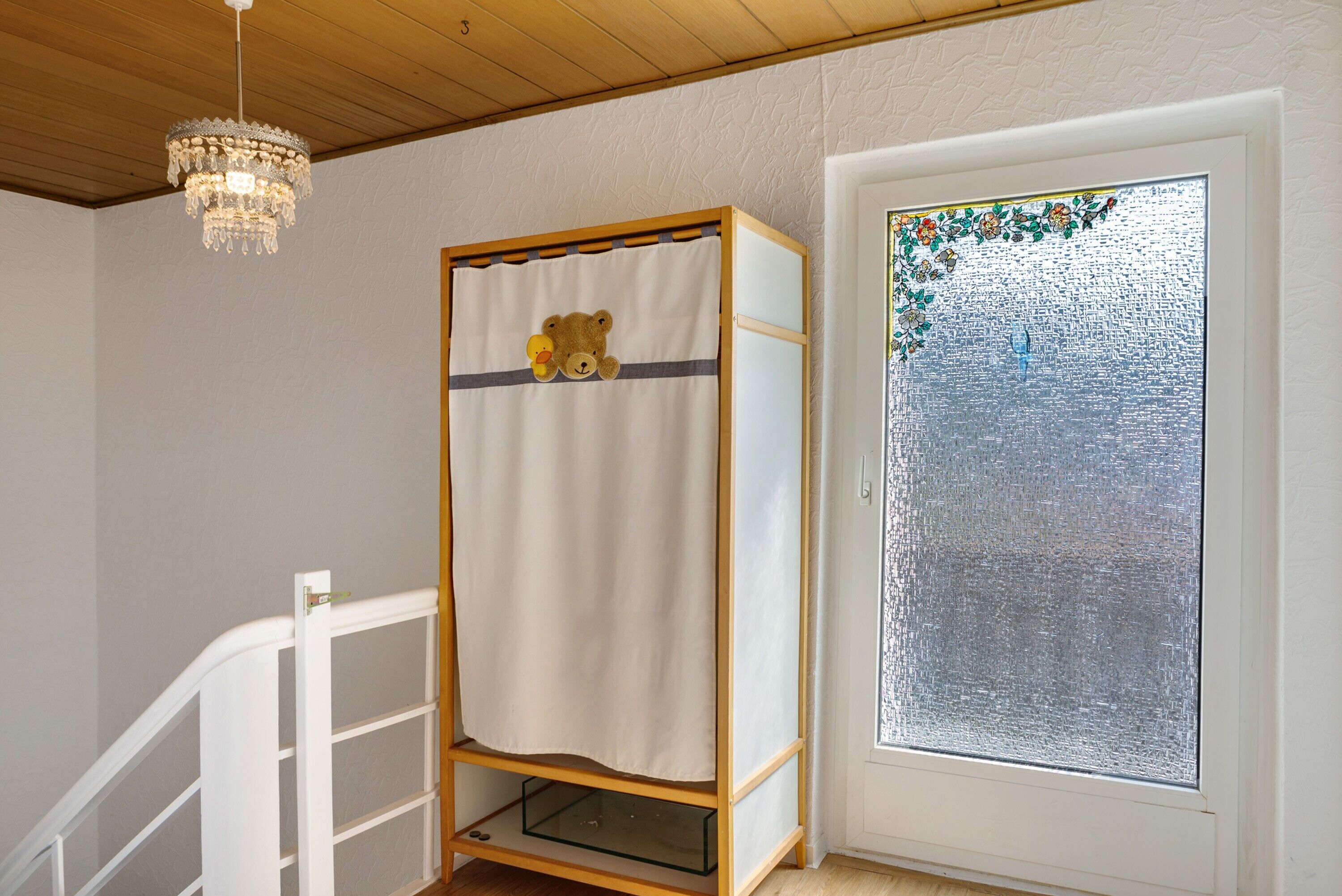 A room with a bunk bed, a chandelier, a glass door with a floral design, and a white staircase.
