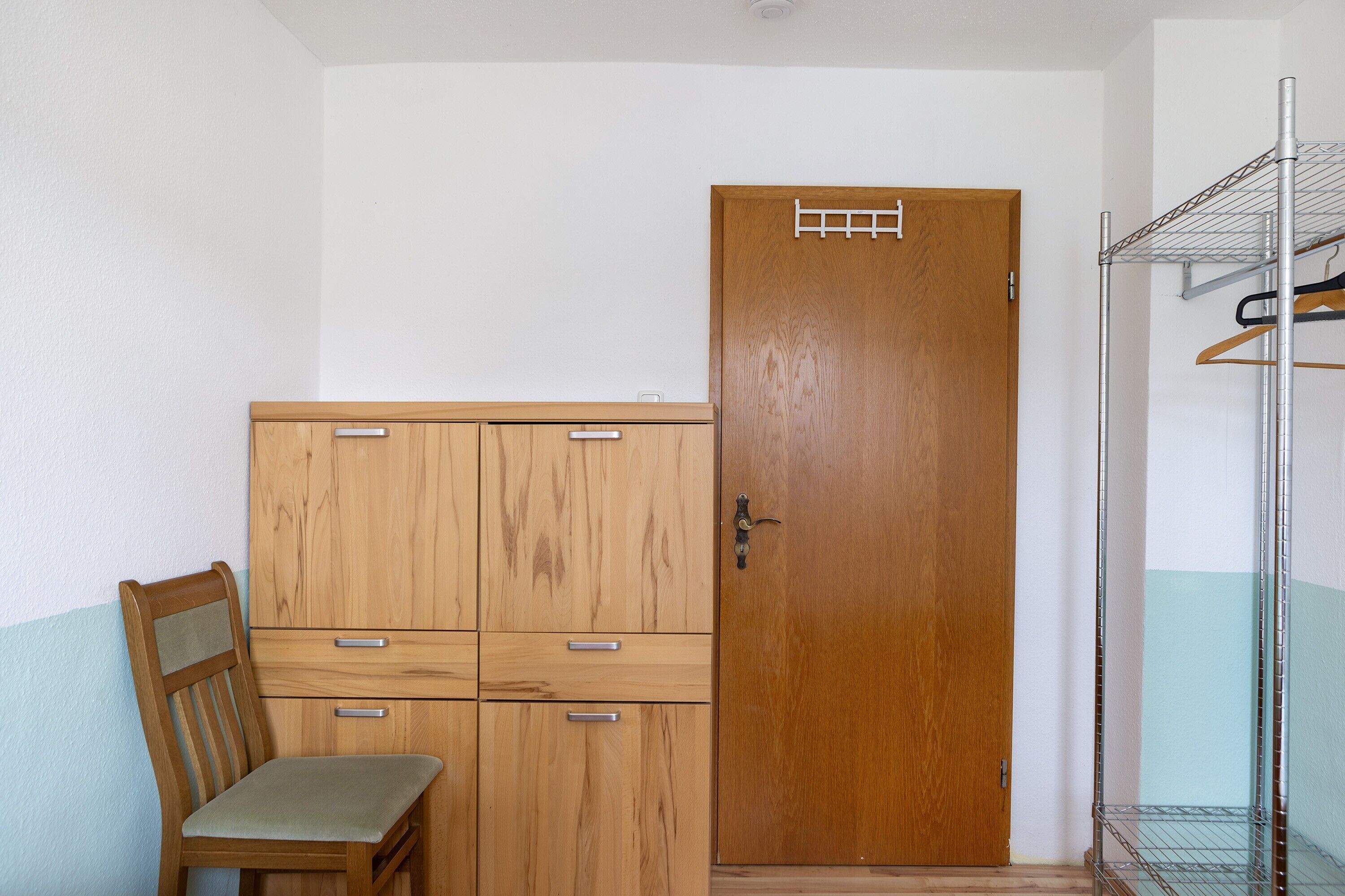 Ein Zimmer mit Holzschrank, einem Stuhl und einer Tür mit Ablage.
