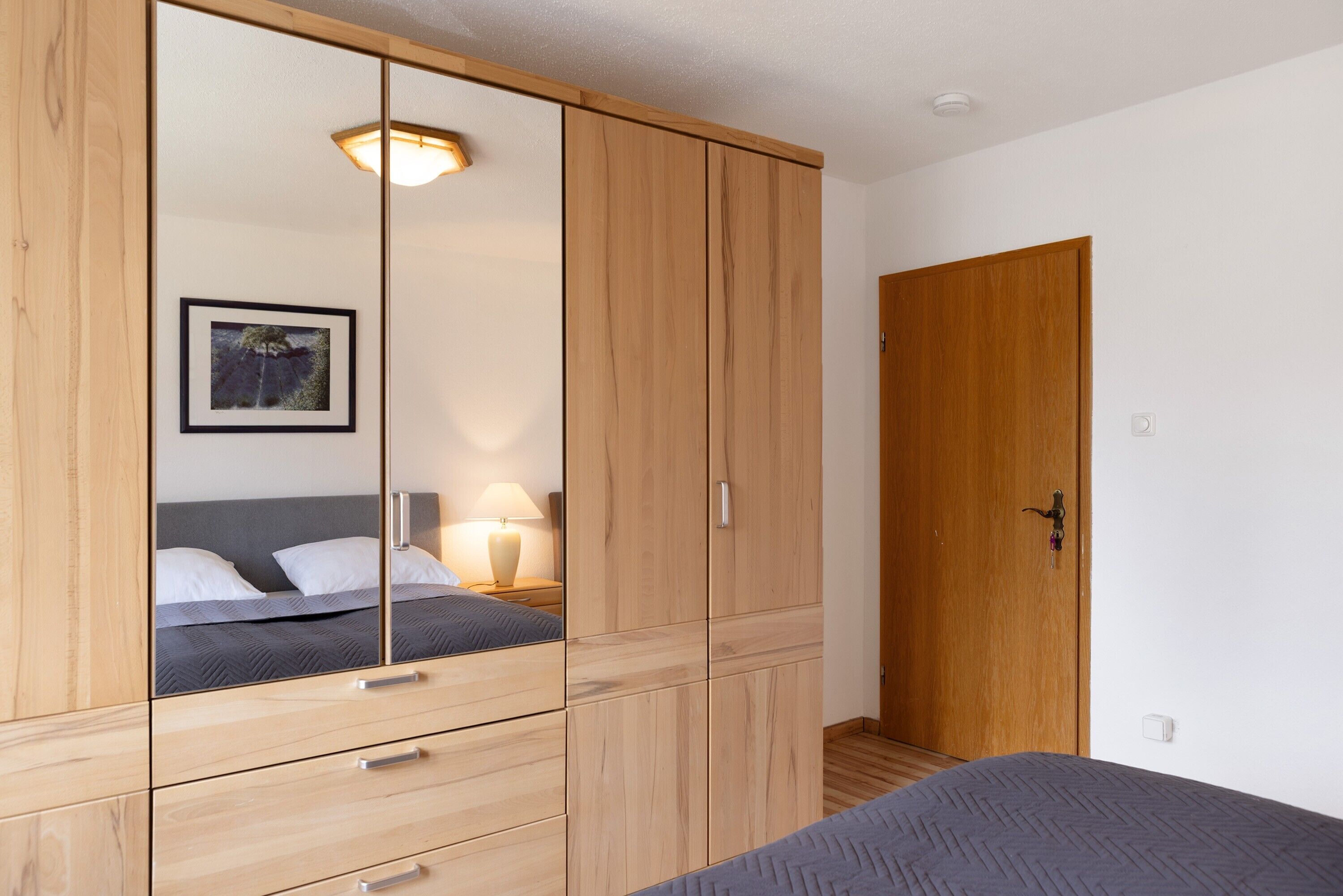 Ein Schlafzimmer mit Bett, Kleiderschrank, Spiegel und einer Tür.