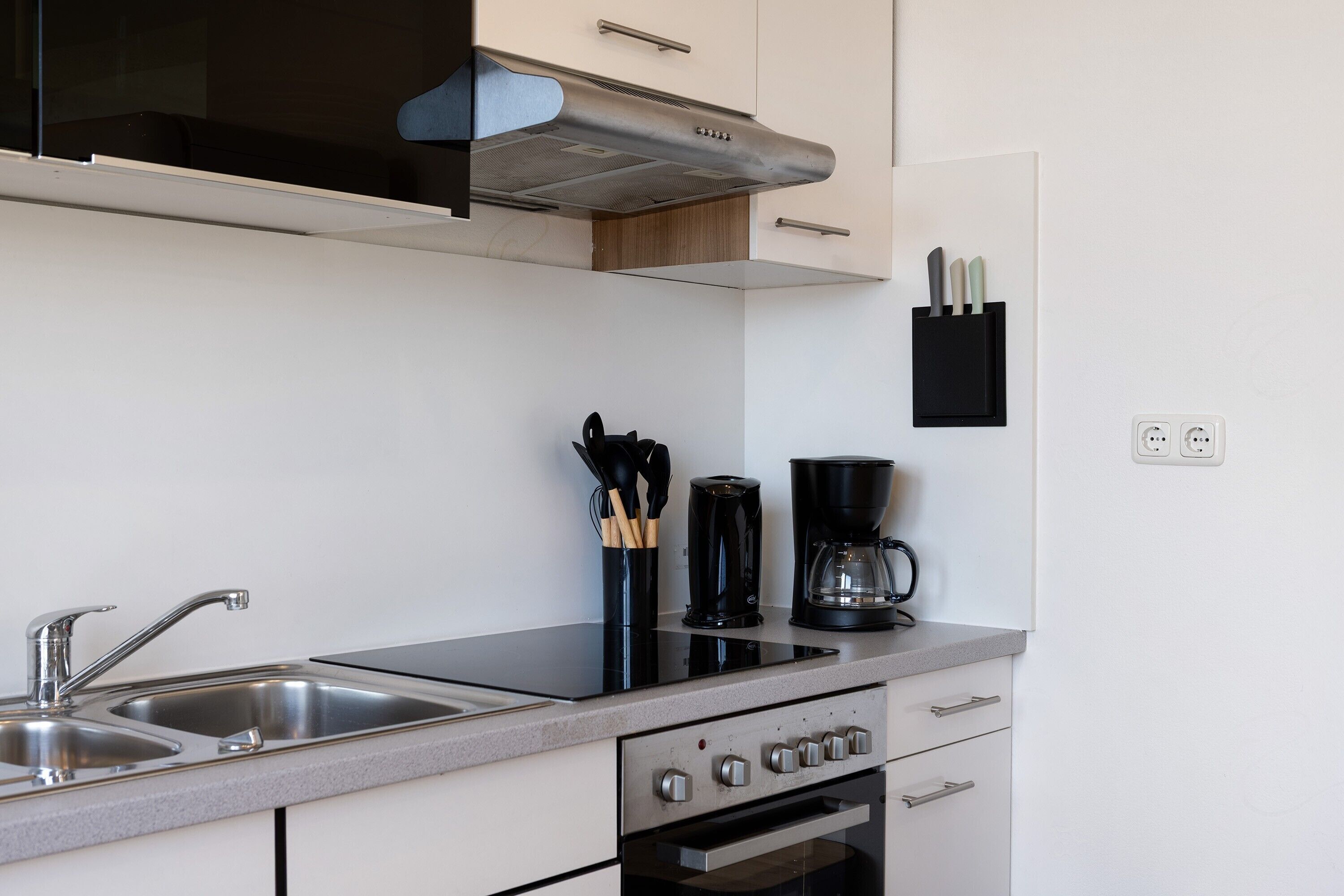Een moderne keuken met een roestvrijstalen spoelbak, een zwarte koffiezetapparaat en een inbouwoven.