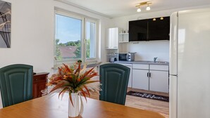 A modern kitchen with white cabinets, a microwave, and a refrigerator. There is a dining table with chairs and a vase of flowers.