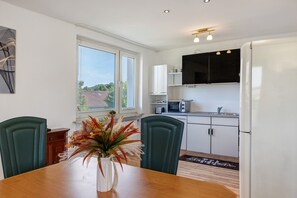 Una cocina moderna con armarios blancos, microondas y refrigerador. Hay una mesa de comedor con sillas y un florero.