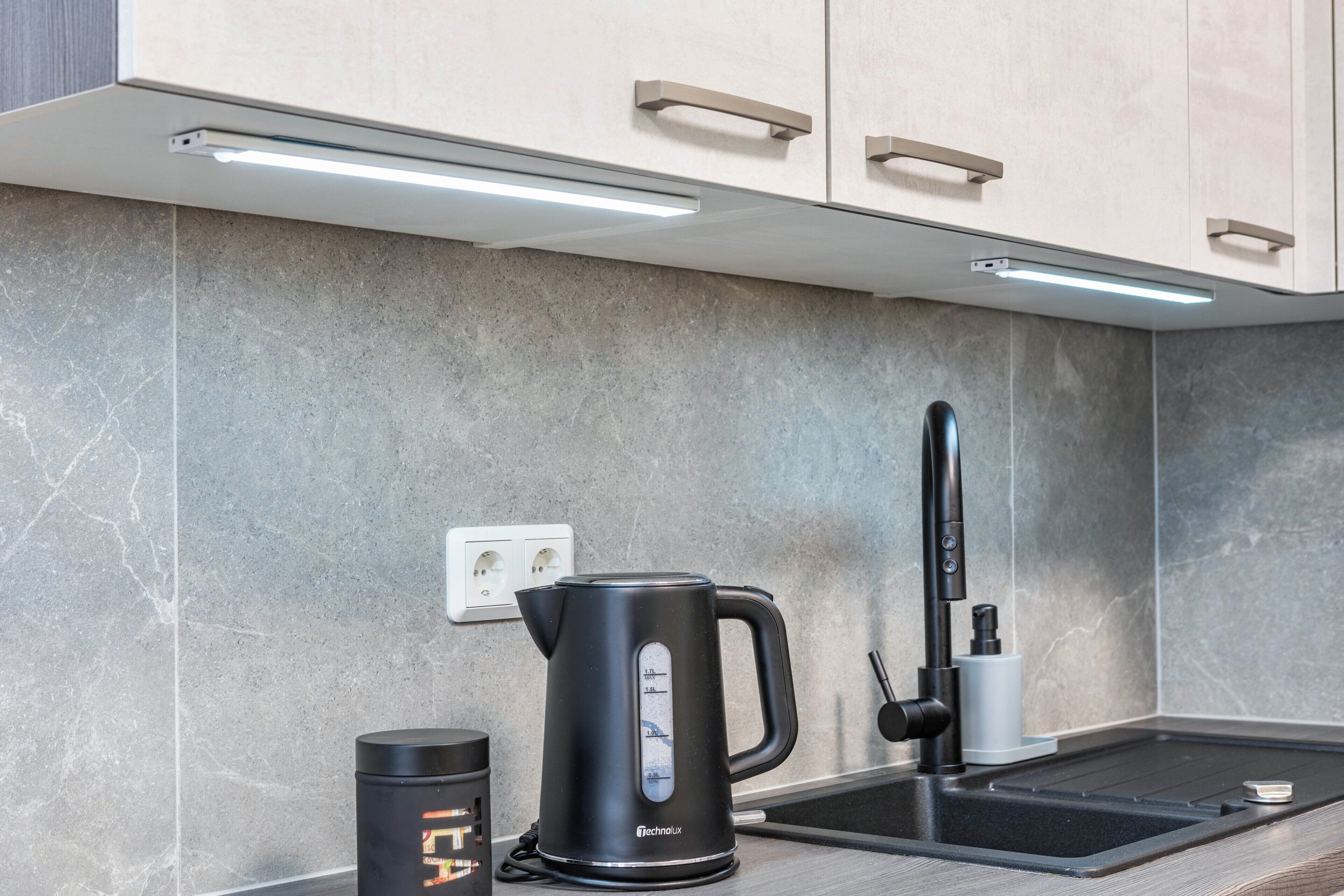 A modern kitchen with a kettle, a coffee maker, and a sink.