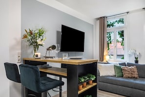 Un salon moderne doté d’un téléviseur à écran plat, d’une table à manger, de deux chaises, d’un canapé et d’une fenêtre avec des rideaux.