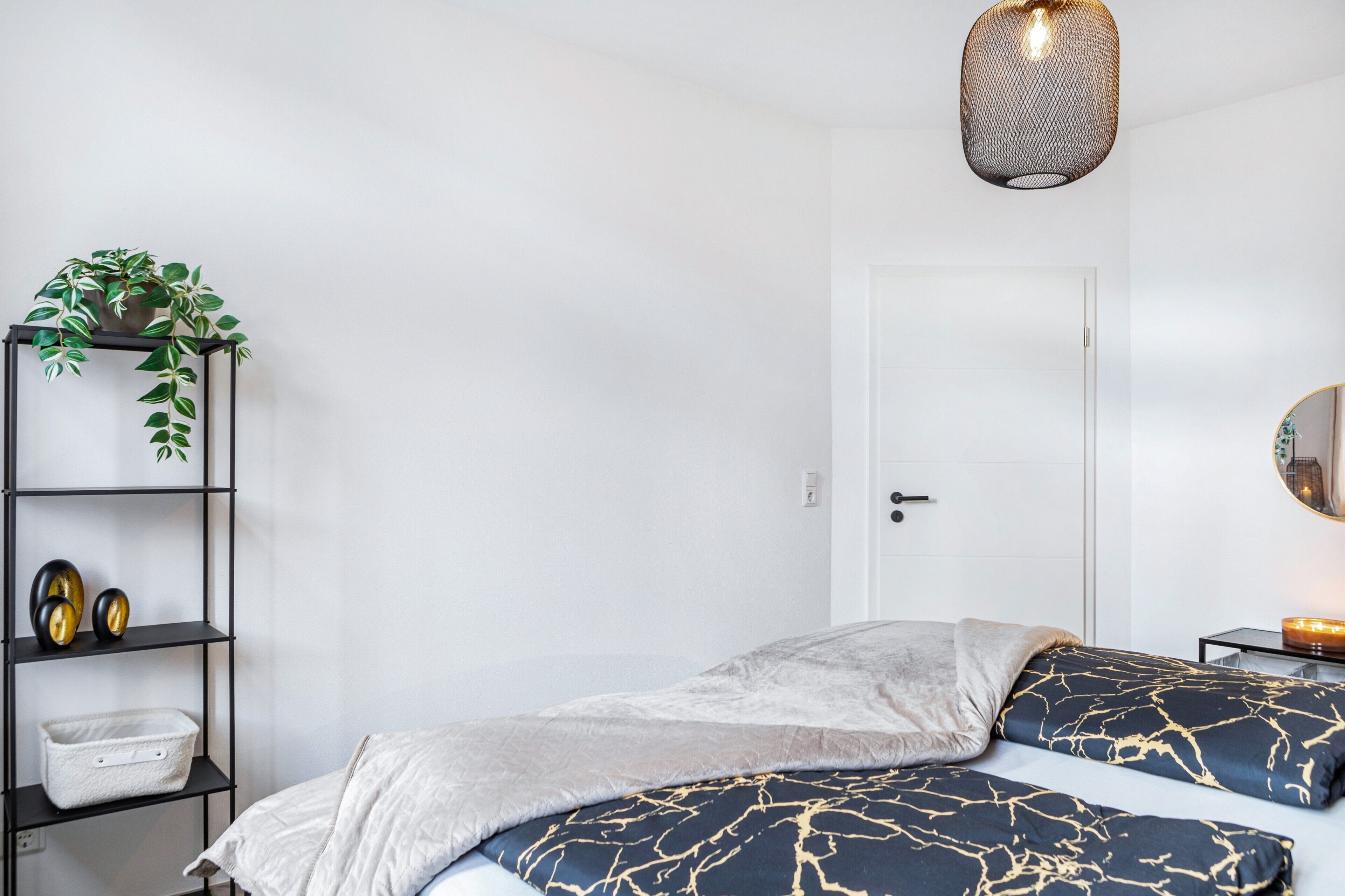 Ein Schlafzimmer mit einem Bett, einem Nachttisch, einem Regal mit Dekoration, einer Pendelleuchte und einer Tür.