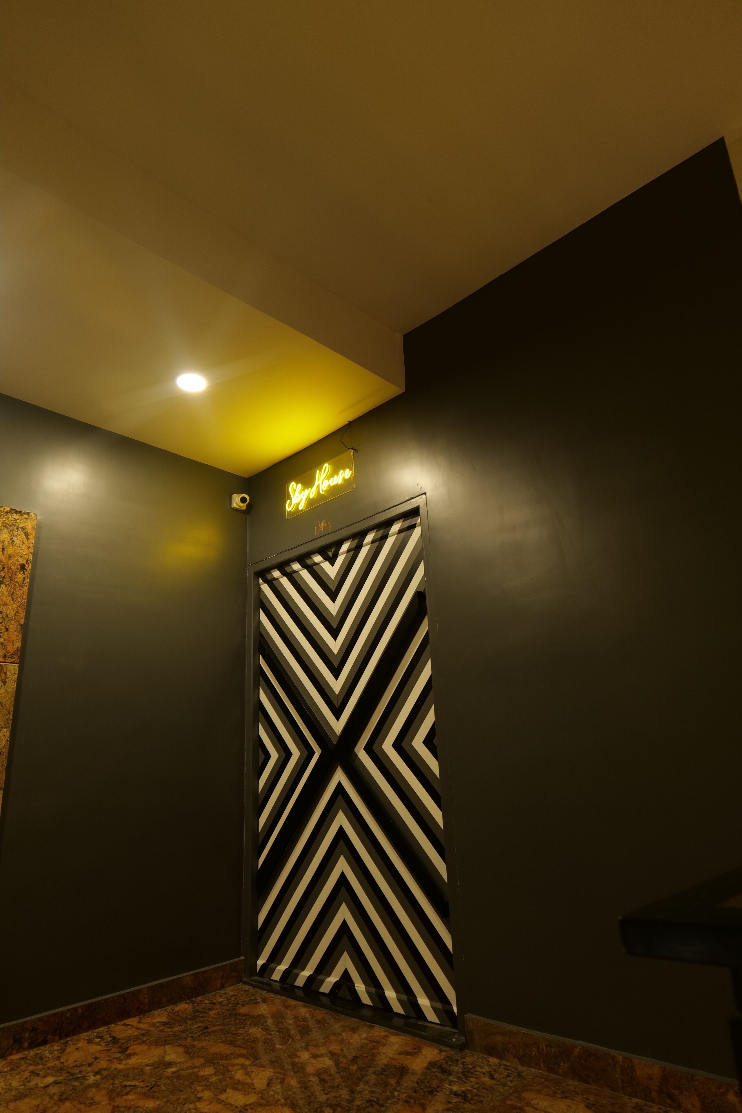 A hallway with a black and white chevron-patterned door, a neon sign reading "Sky House", and a marble floor.