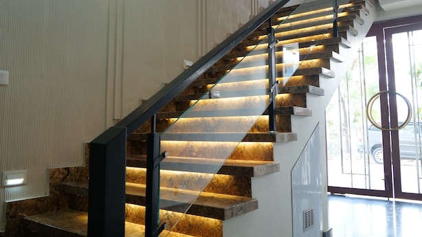 Una escalera moderna con barandilla metálica y peldaños iluminados, que conduce a una plataforma con puerta de vidrio.