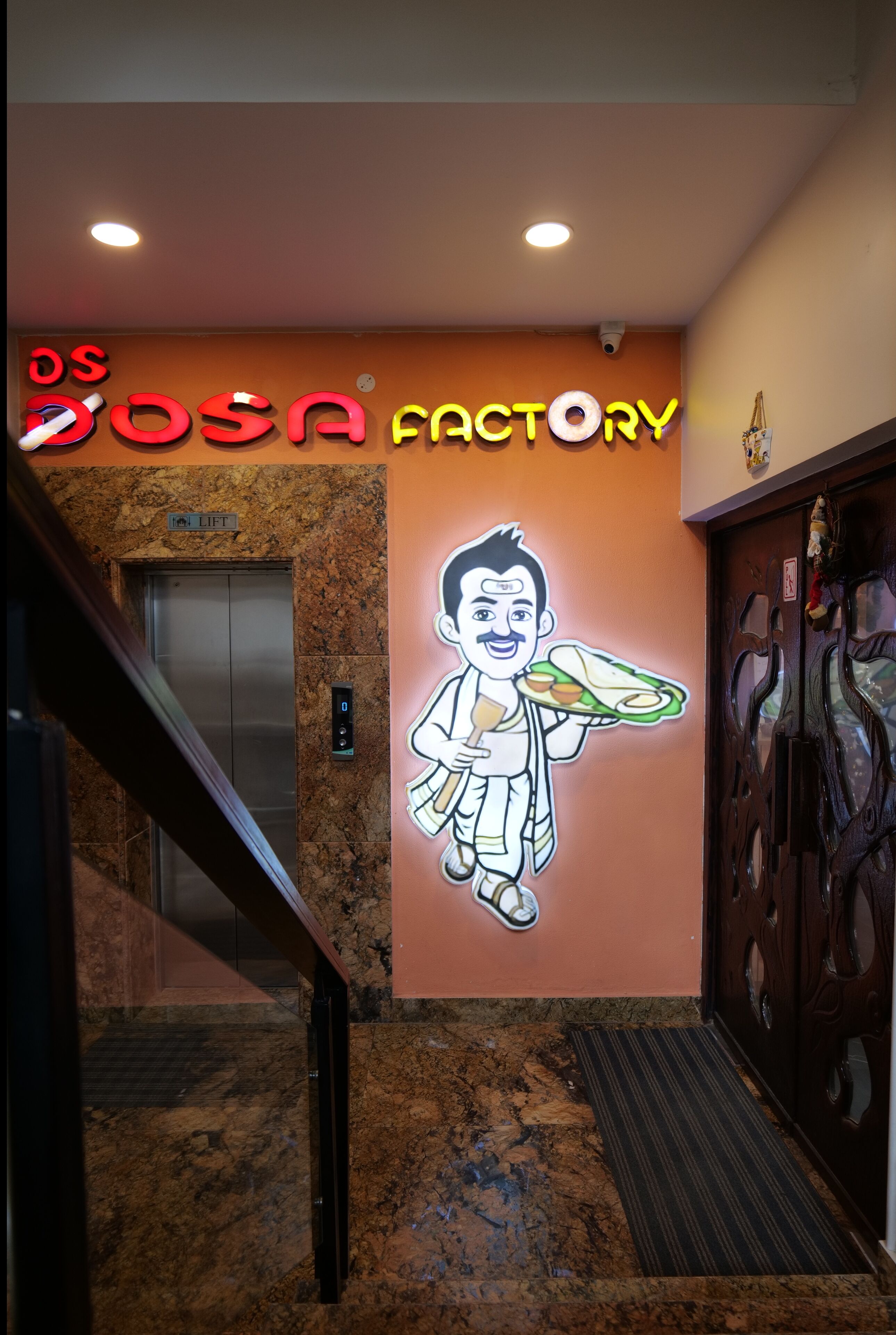 Seinä, jossa on neonvalomainos, jossa lukee ”OSOSA FACTORY”, ja sarjakuvahahmo, joka pitää kädessään lautasen.