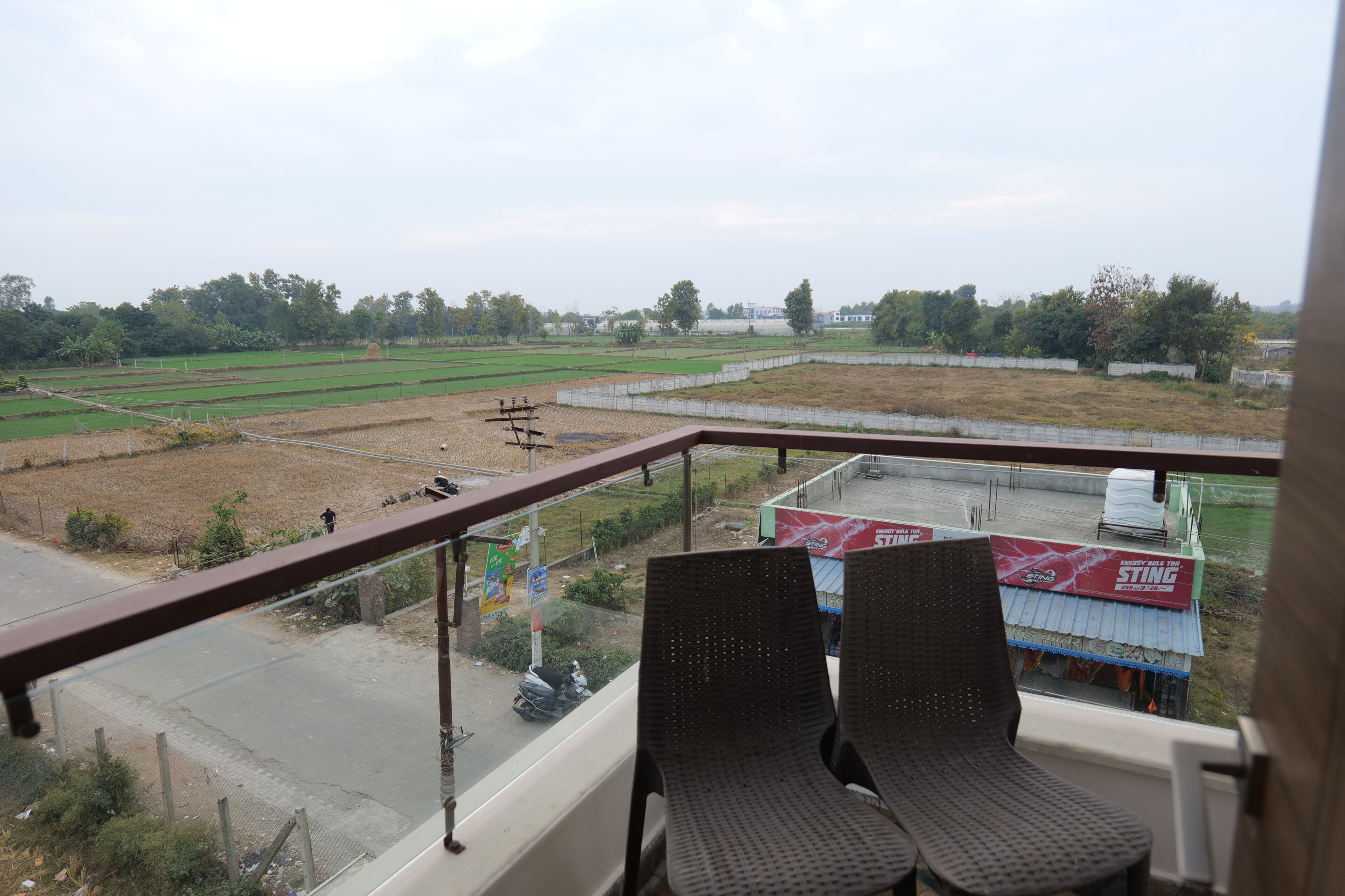 Un balcon avec deux chaises, une vue sur un champ verdoyant et un bâtiment avec une enseigne rouge.