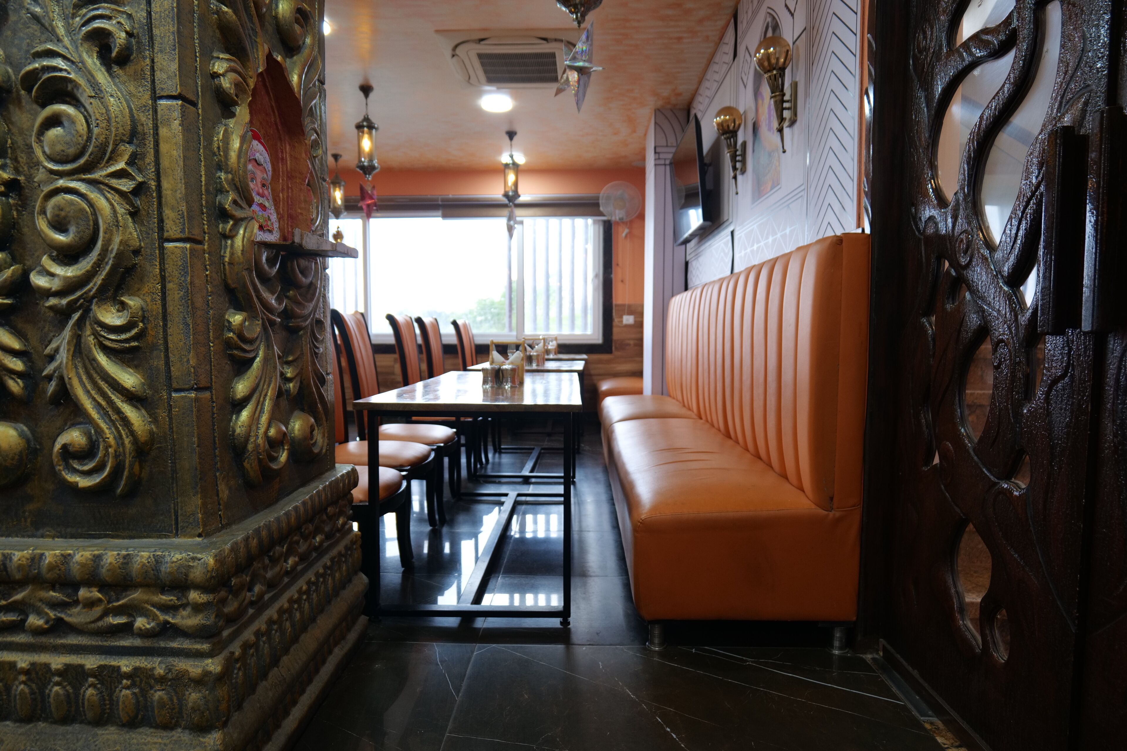 Un restaurant doté d’une longue table, de banquettes orange, de boiseries décoratives et de luminaires suspendus.