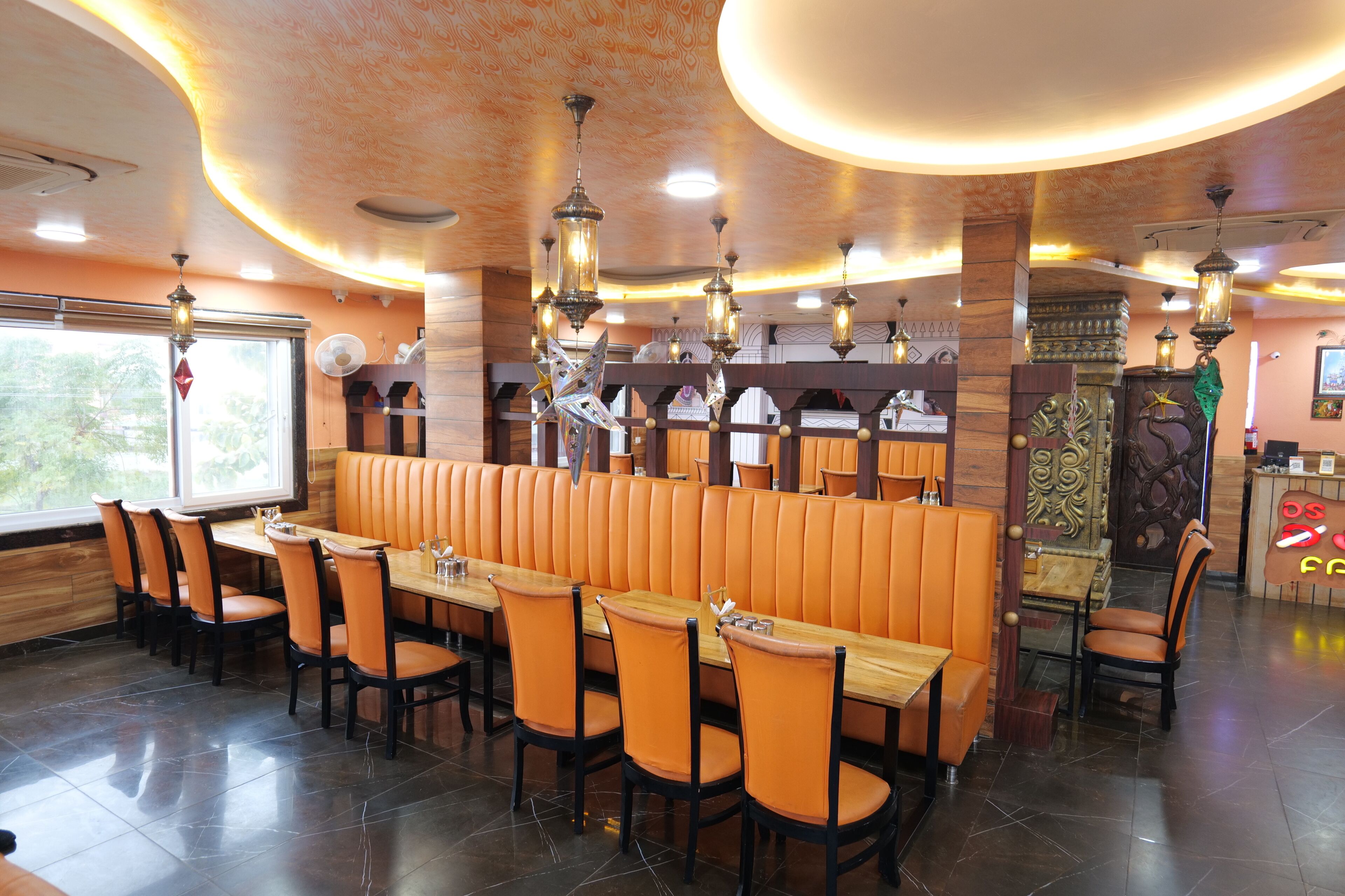 Un restaurante con mesas de madera y asientos tapizados en naranja, que presenta un diseño de techo moderno e iluminación ambiental.