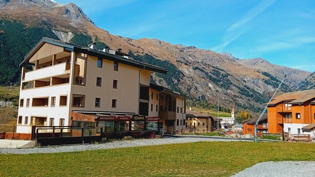 A multi-story building with a restaurant on the ground floor, set against a mountainous backdrop. - Terrasses D 501 - Parc Nat. Vanoise Appart. 5 Pers (Val-Cenis)