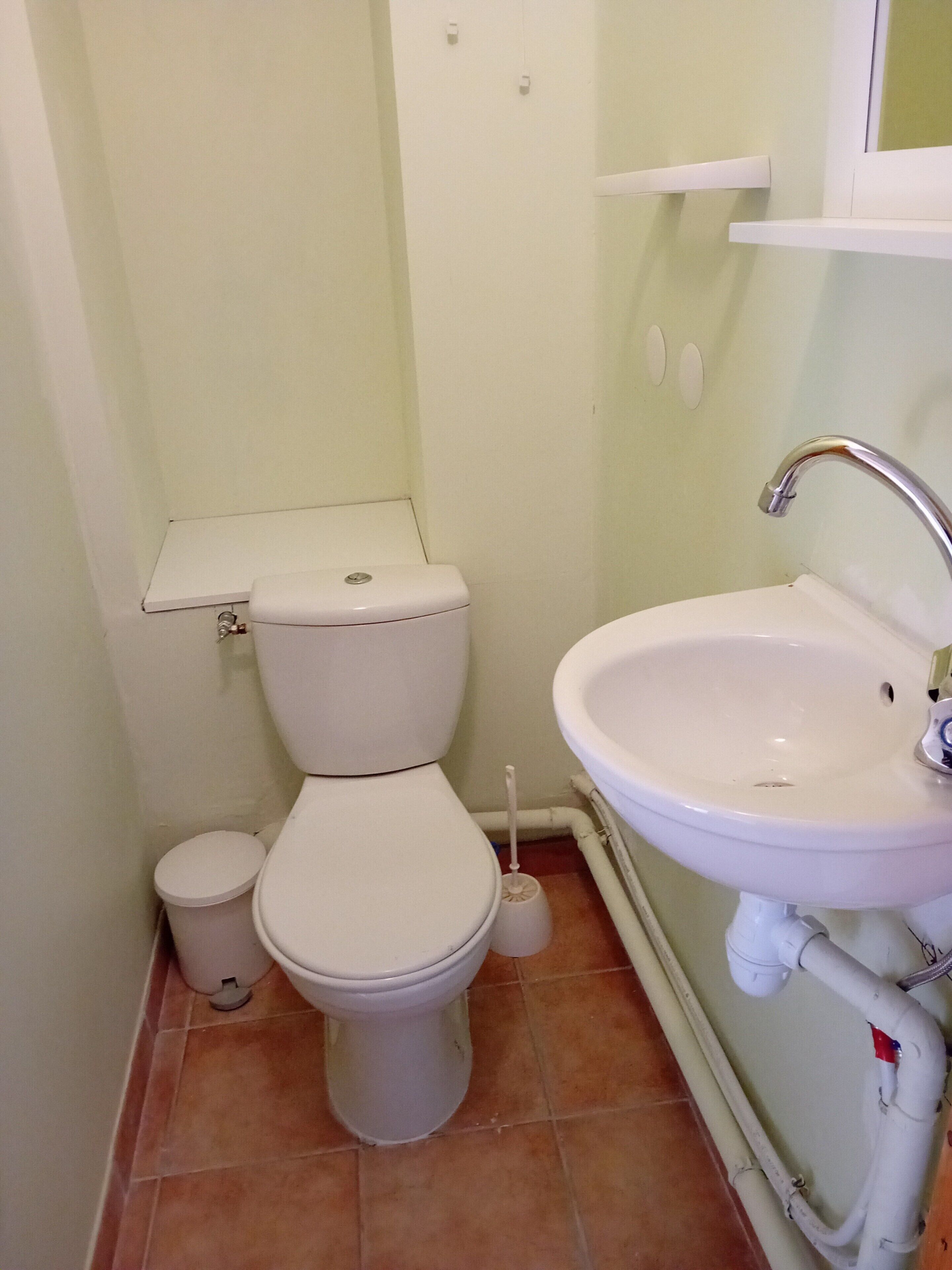 Un baño pequeño con inodoro, lavamanos y escobilla.
