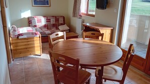 A cozy room with a wooden dining table and chairs, a sofa with patterned cushions, a television mounted on the wall, and a window with a view of a green landscape. - Terrasses D 501 - Parc Nat. Vanoise Appart. 5 Pers (Val-Cenis)