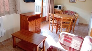 A room with a wooden dining table, chairs, a wooden cabinet, a television, a microwave, and a window with curtains. - Terrasses D 501 - Parc Nat. Vanoise Appart. 5 Pers (Val-Cenis)