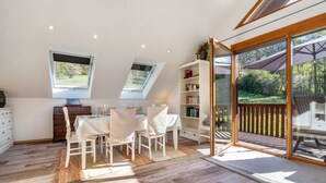 A dining area with a table and chairs, a bookshelf, and a large sliding glass door leading to an outdoor deck. - Holiday Home with Mountain View, Large Terrace and Wi-Fi (Baden-Baden)