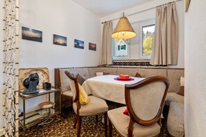 A dining area with a table, chairs, a lamp, a coffee machine, and artwork on the wall.