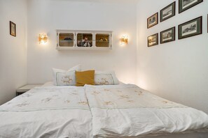 A bedroom with a bed, a nightstand, a wall-mounted cabinet, and framed pictures on the wall.