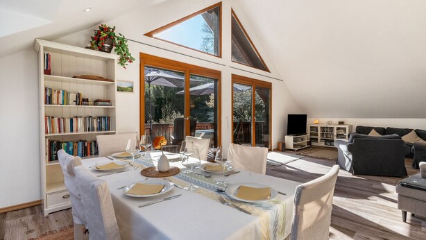 A dining area with a table set for four, a bookshelf, and a view of the outdoors. - Holiday Home with Mountain View, Large Terrace and Wi-Fi (Baden-Baden)