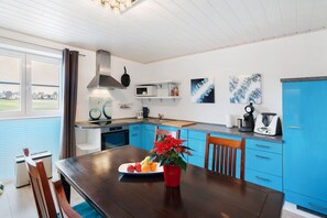 A modern kitchen with blue cabinets, a wooden dining table, and a red flower vase.