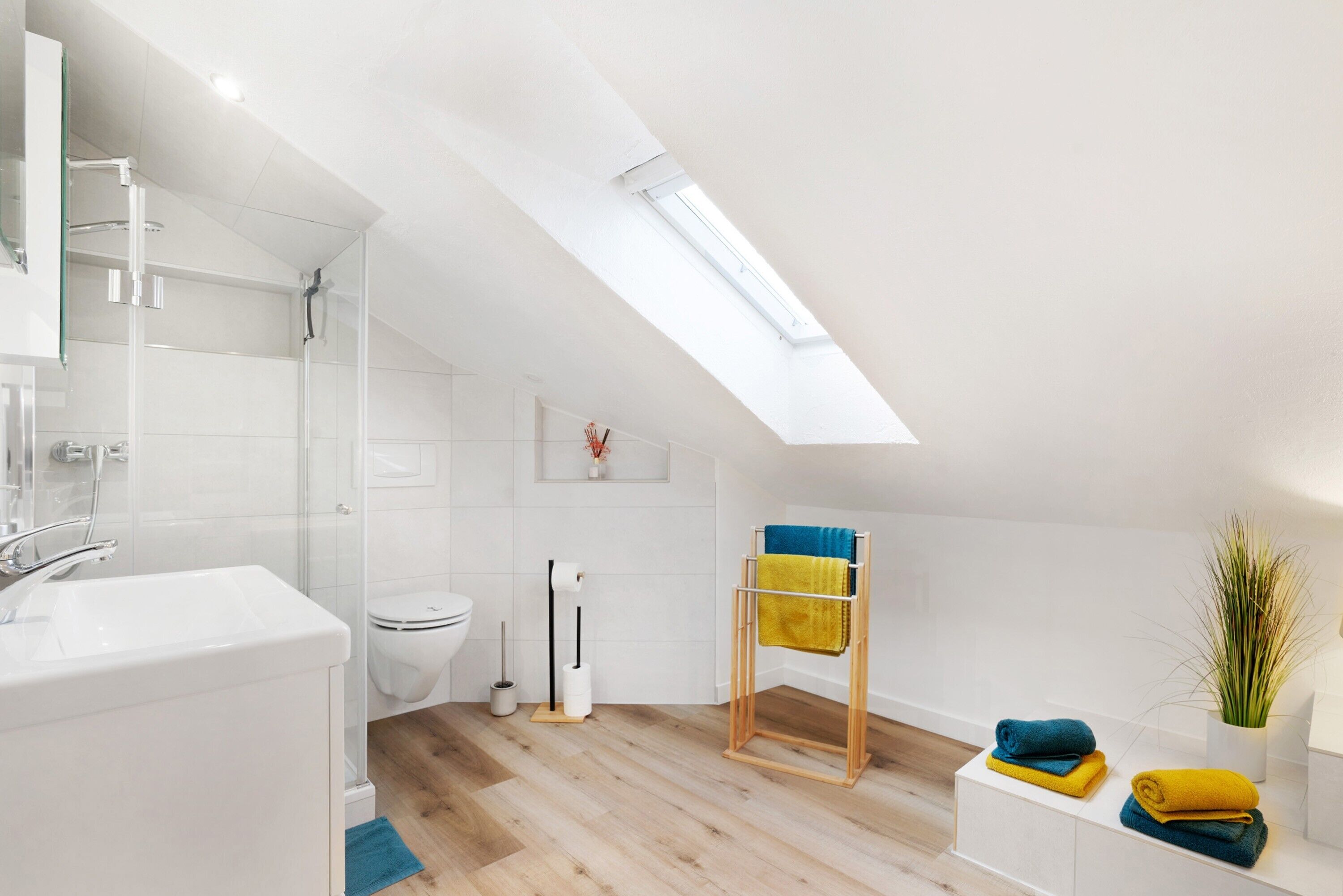 A modern bathroom with a skylight, a glass shower enclosure, a toilet, and a wooden towel rack.